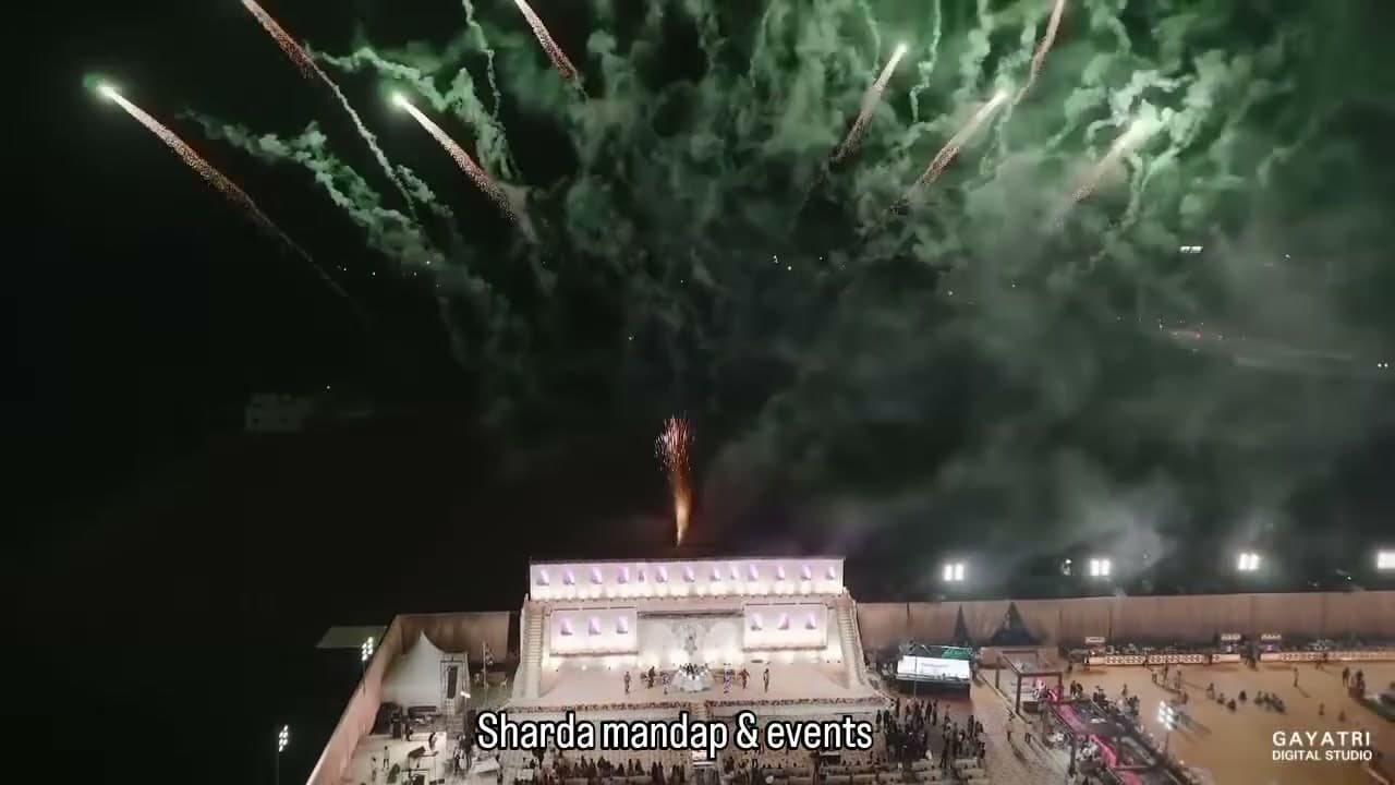 Fireworks bursting over the towering illuminated palace-style reception facade at night, viewed from above the venue.