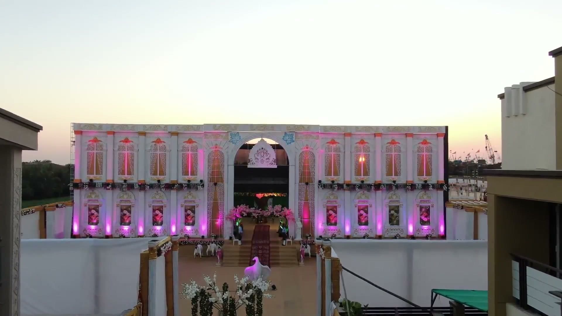 A two-storey illuminated palace-style reception facade in pink and gold light at dusk, with a floral archway entrance and red carpet