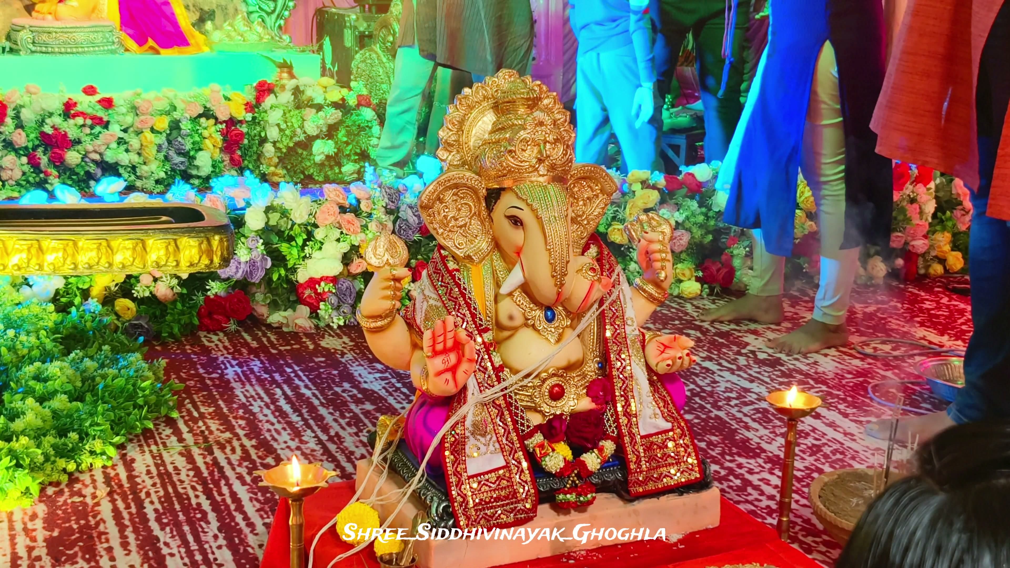 Gold-crowned Ganesh idol dressed in red and gold seated before a wall of fresh floral garlands