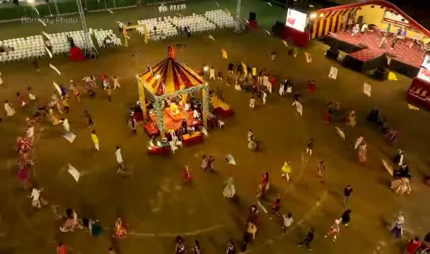 Aerial drone view directly overhead of the floral canopy centerpiece ringed by hundreds of garba dancers at night