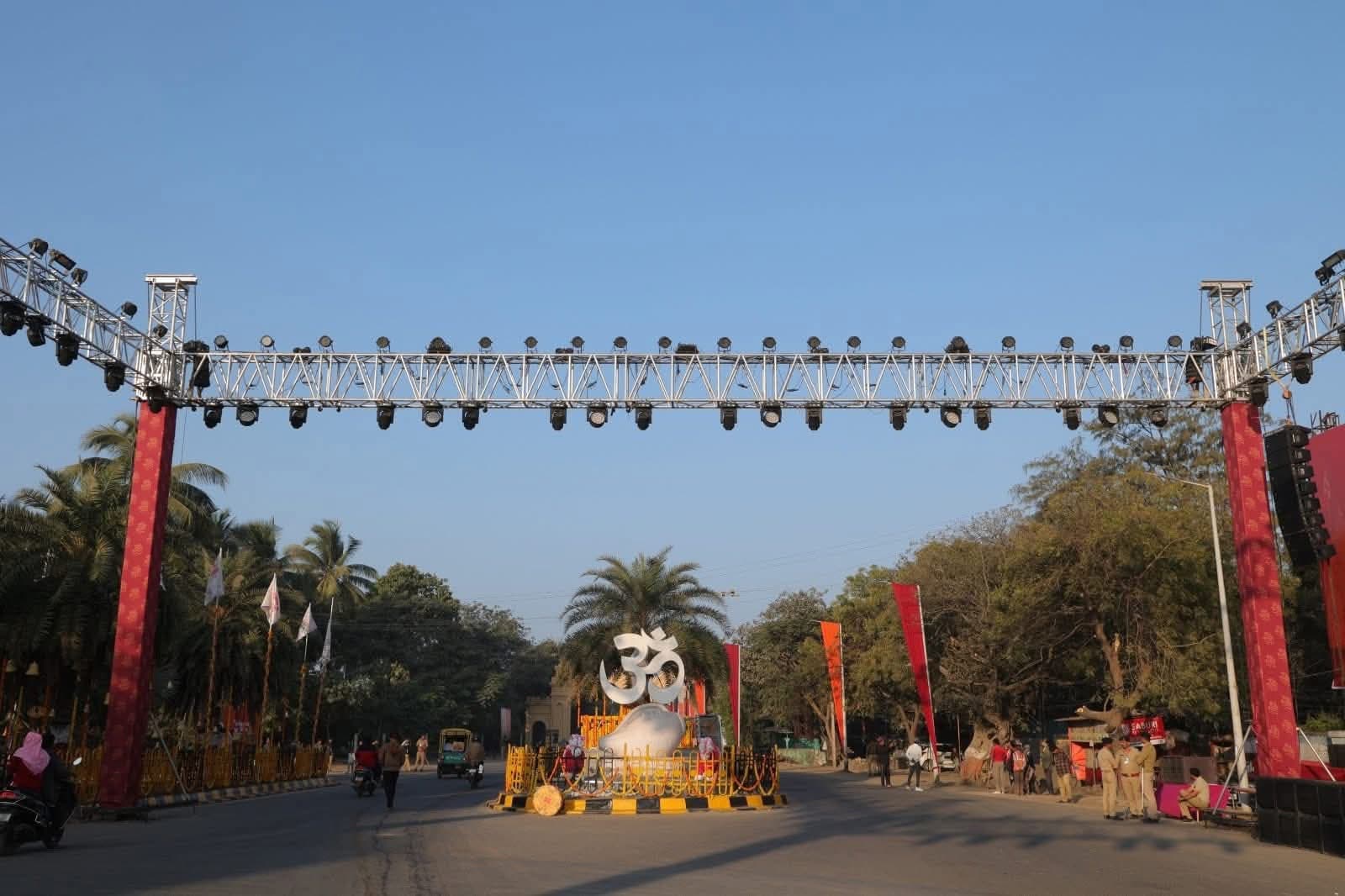 Truss lighting gate spanning the road into Somnath, centered on a large illuminated Om sculpture