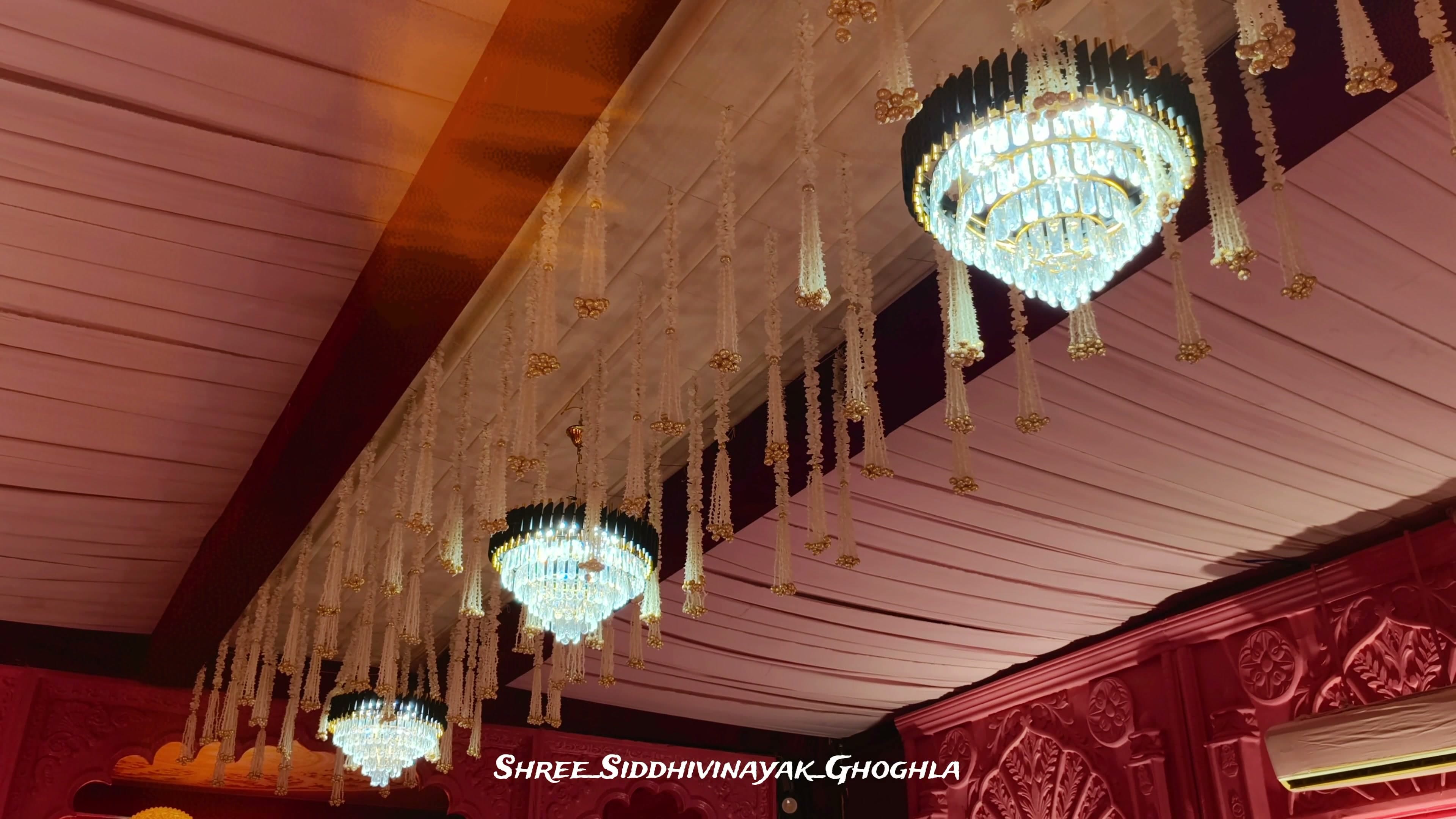 Crystal chandeliers hung with strands of white flowers beneath a rose-pink draped ceiling
