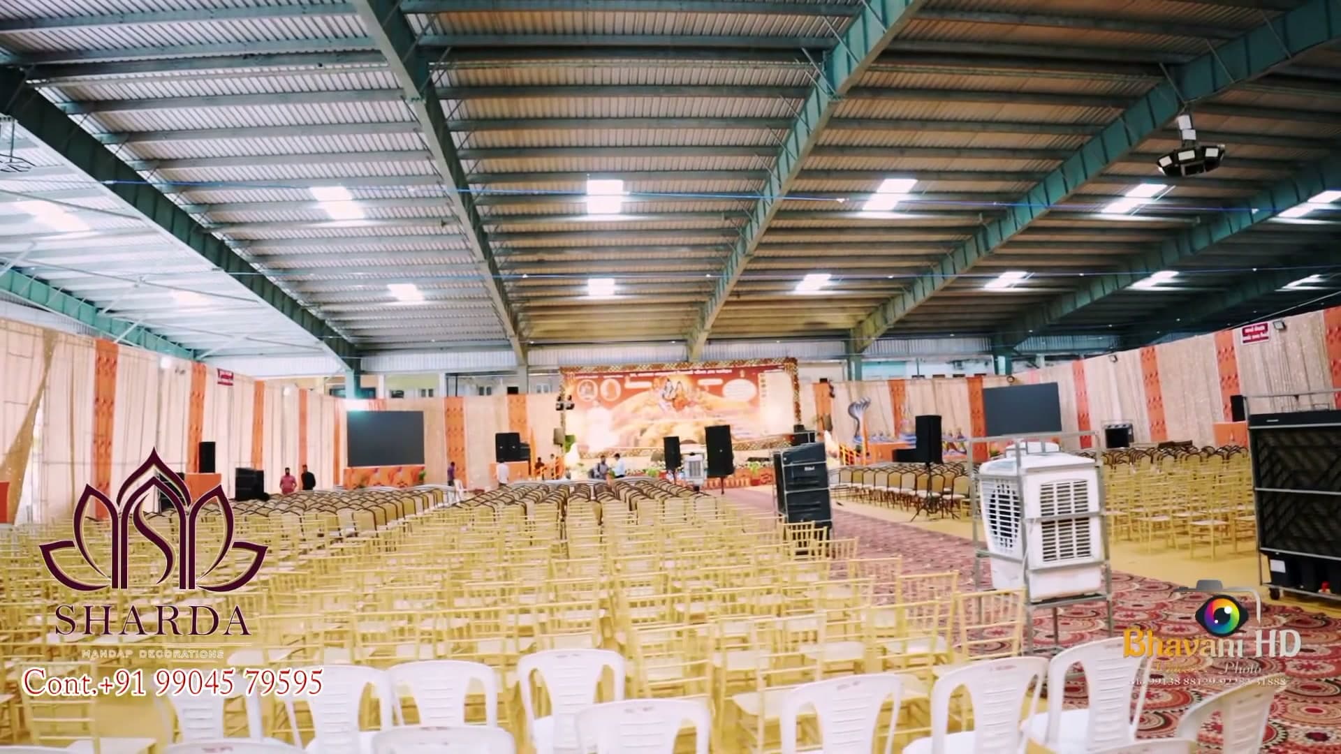 Full interior view of the decorated hall for the Shiv Mahapuran katha, rows of gold and white chairs facing a red-and-gold stage backdrop, sequin drape walls on either side.