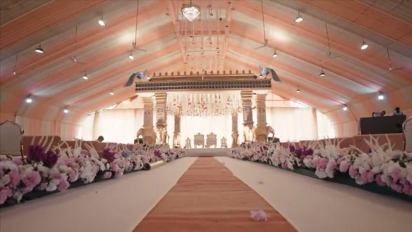 Peach and white striped canopy hall with a long aisle lined in pink, purple and white flowers leading to a stage of golden pillars and chandeliers — Mangrol Bandar, Gujarat
