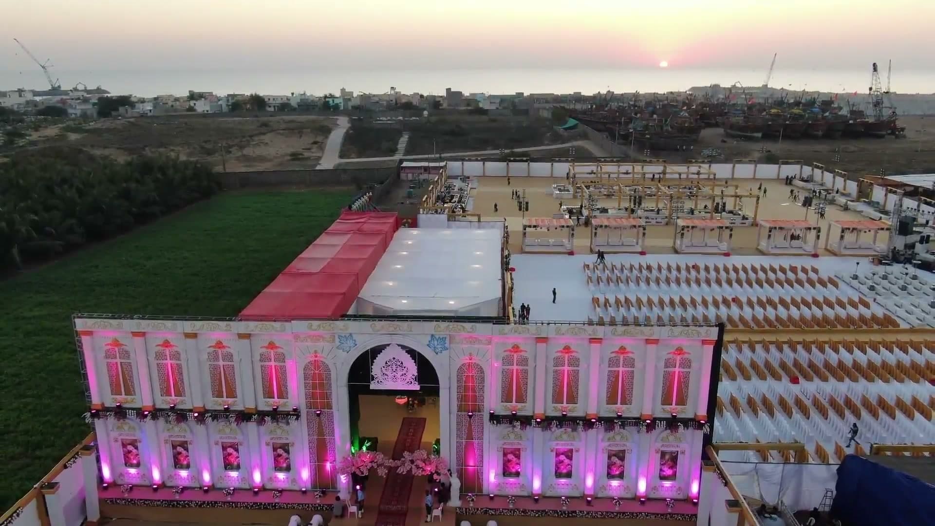 Aerial view of the reception venue at Mangrol Bandar, Gujarat, showing guest seating, lounge cabanas, and the harbor's fishing fleet at sunset