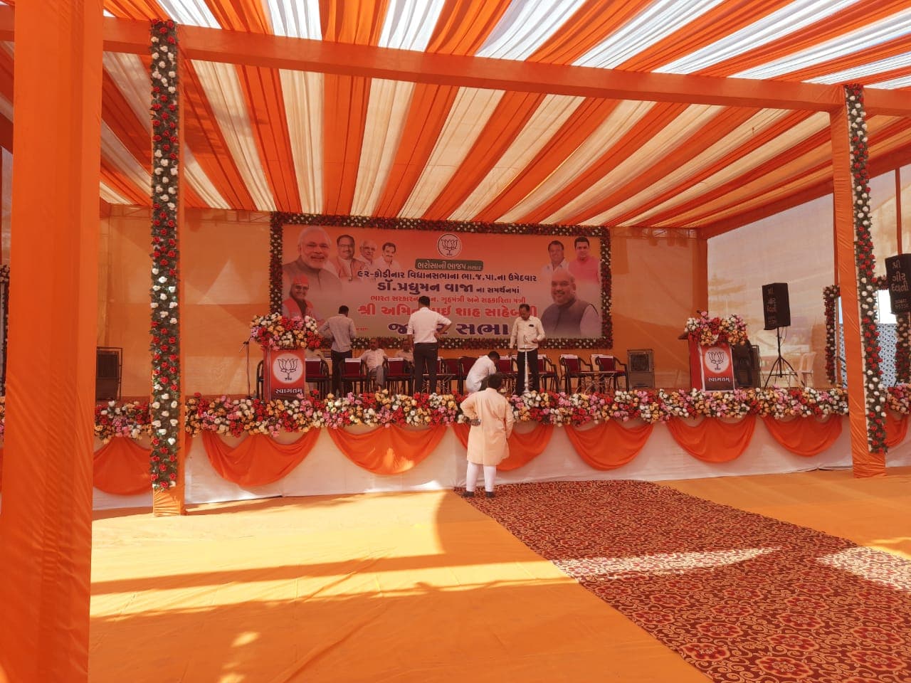 Stage backdrop dressed with fresh floral garlands and drapery ahead of a public meeting