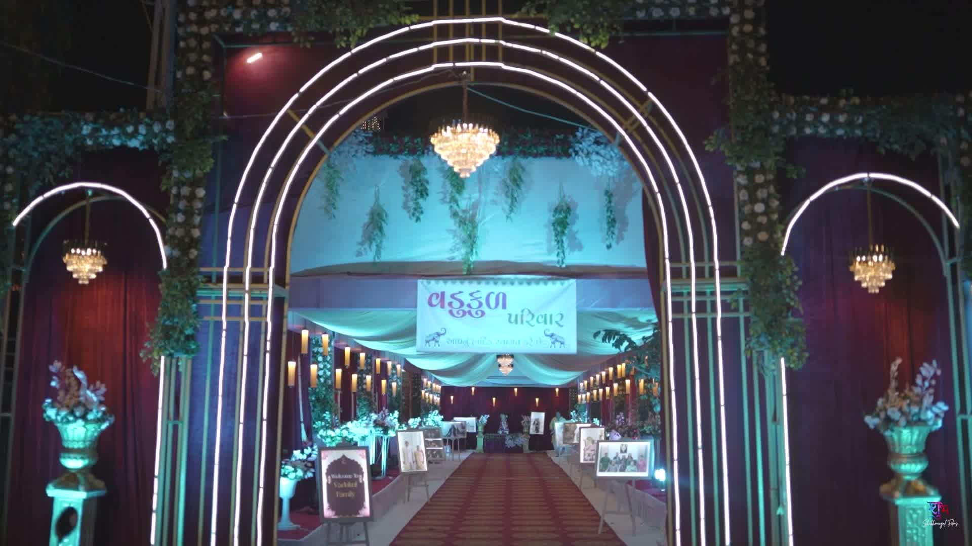 Arched welcome corridor lined with glowing lights, floral garlands, and hanging chandeliers leading guests toward the stage